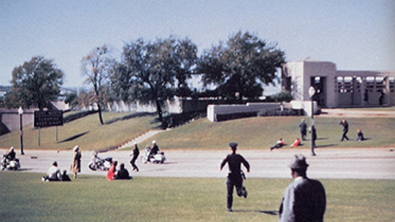 Film frame from home movie footage shot by Mark Bell on November 22, 1963, seconds after the Presidential motorcade had passed. The grassy knoll, from which many witnesses heard gunshots, is in the background. (Courtesy of Rauner Special Library)